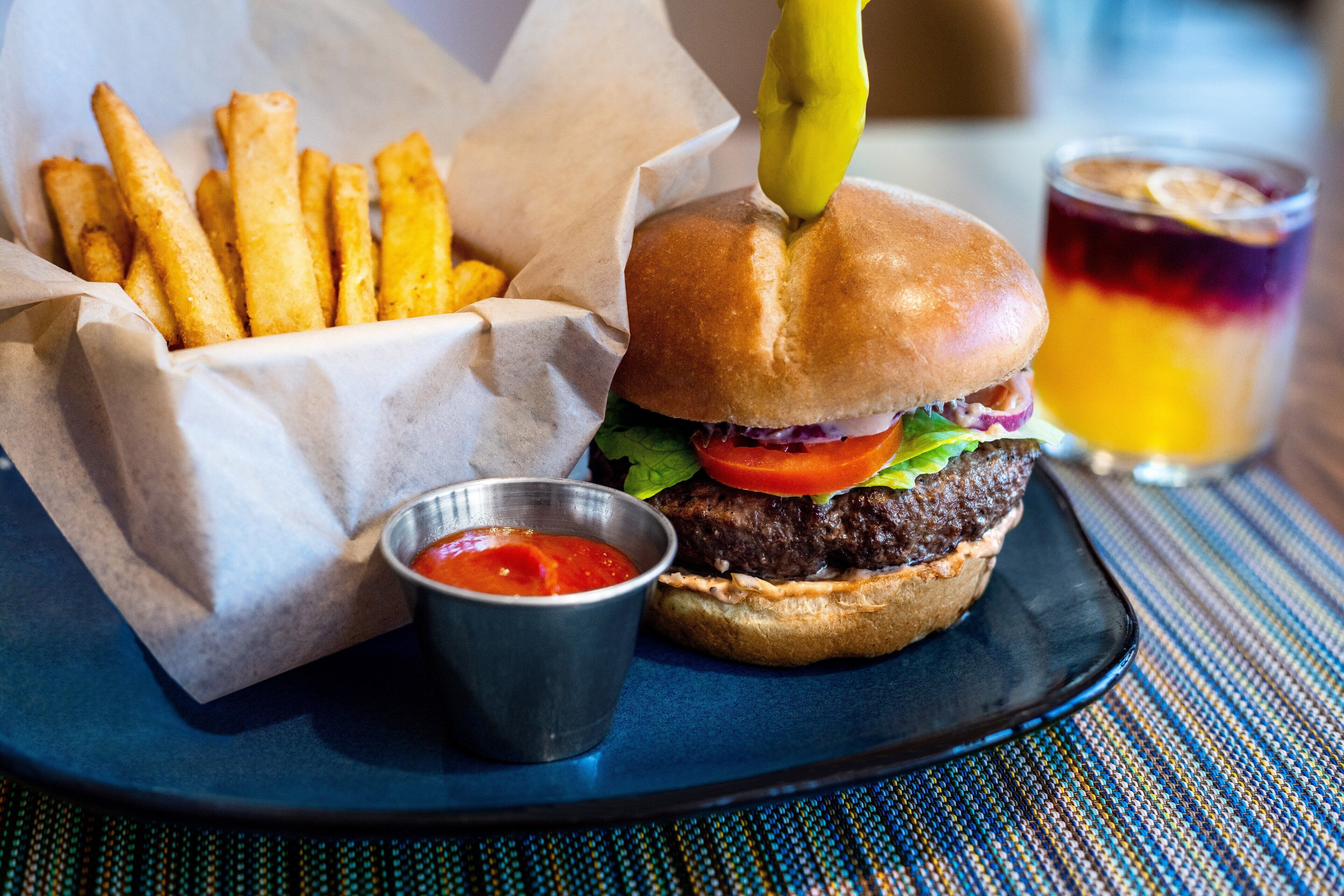 A burger with fries and a drink on a plate.