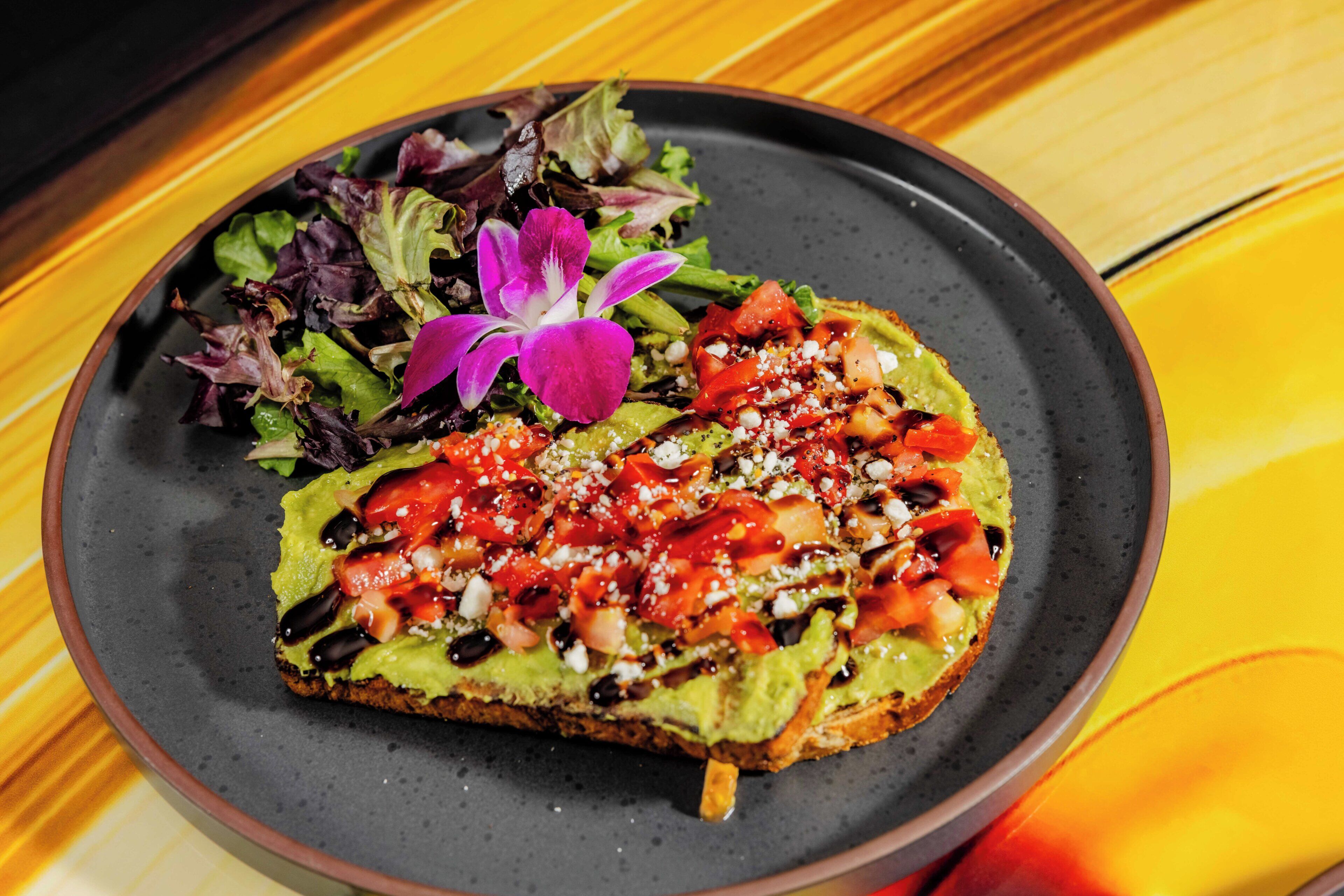 Un plato con un sándwich, ensalada y una flor morada.
