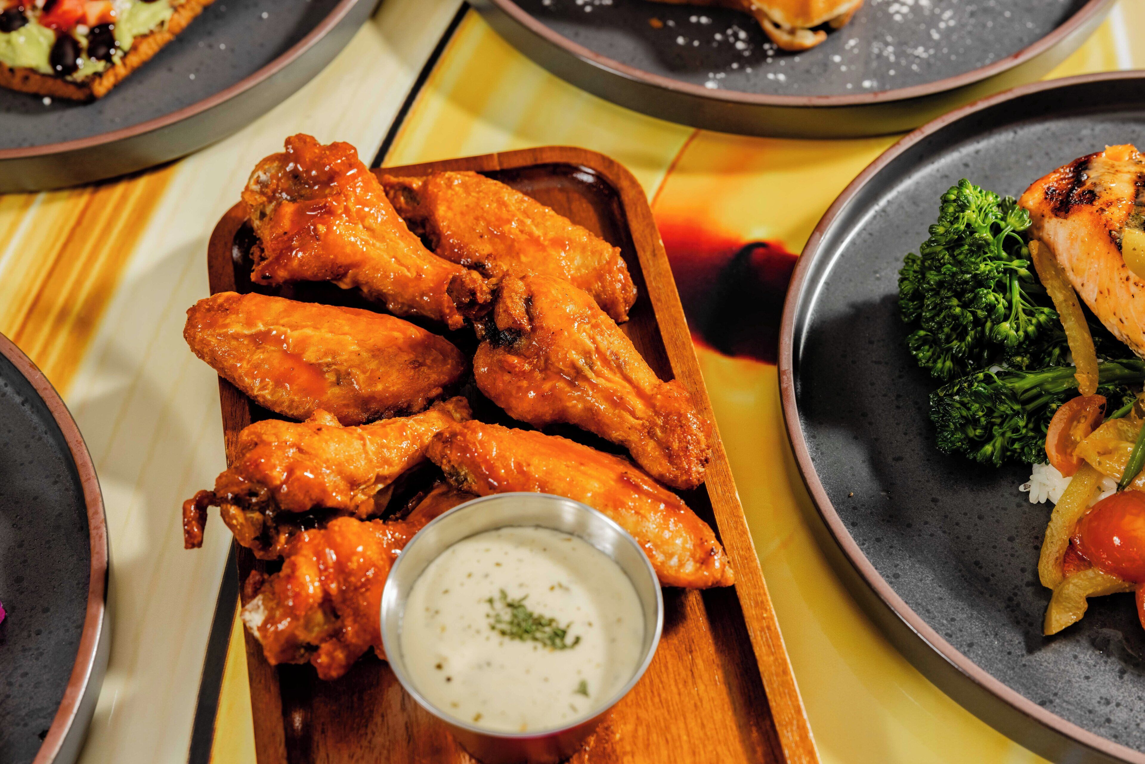 A wooden tray with wings and a small bowl of sauce.