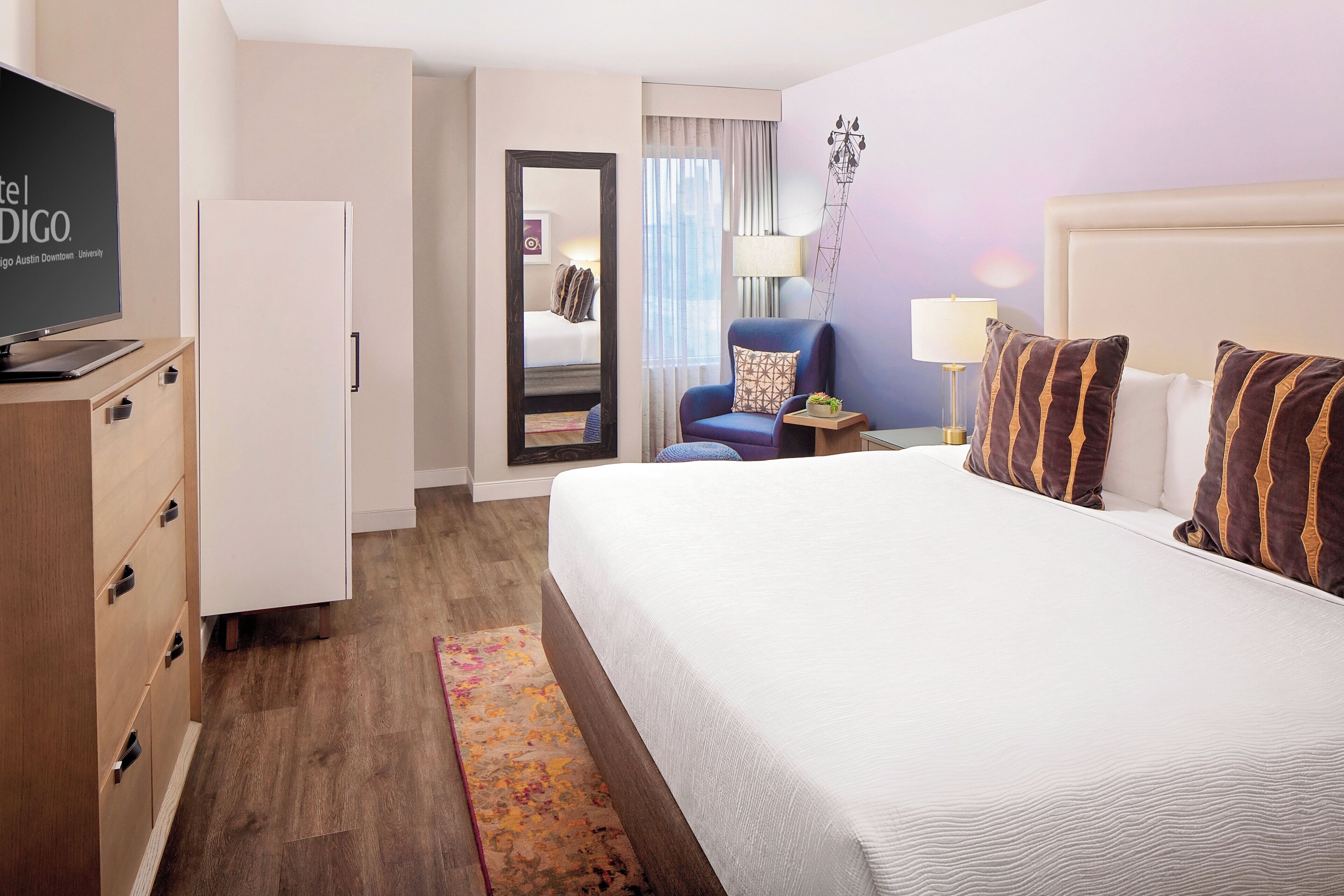 A hotel room with a bed, a TV, a desk, a chair, and a wardrobe.