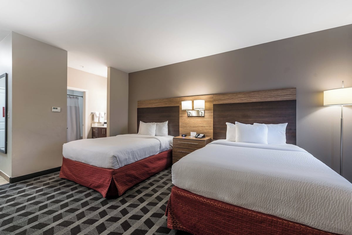 A hotel room with two beds, a wooden headboard, a nightstand, and a lamp.