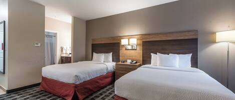 A hotel room with two beds, a wooden headboard, a nightstand, and a lamp.