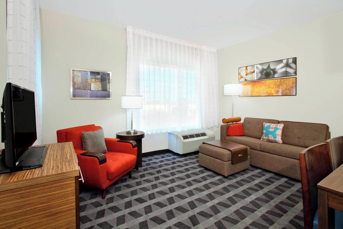 A modern living room with a red armchair, a brown sofa, a wooden coffee table, and a flat-screen TV.