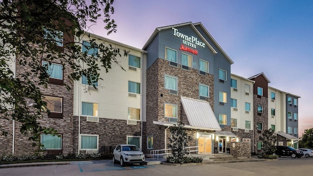 A TownePlace Suites by Marriott hotel with a modern design, featuring multiple floors, large windows, and a parking lot.