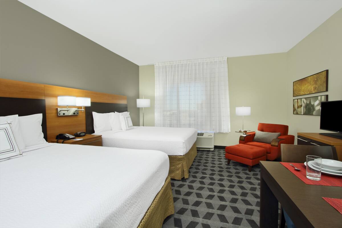 A hotel room with two beds, a desk, a chair, a TV, and a window with curtains.