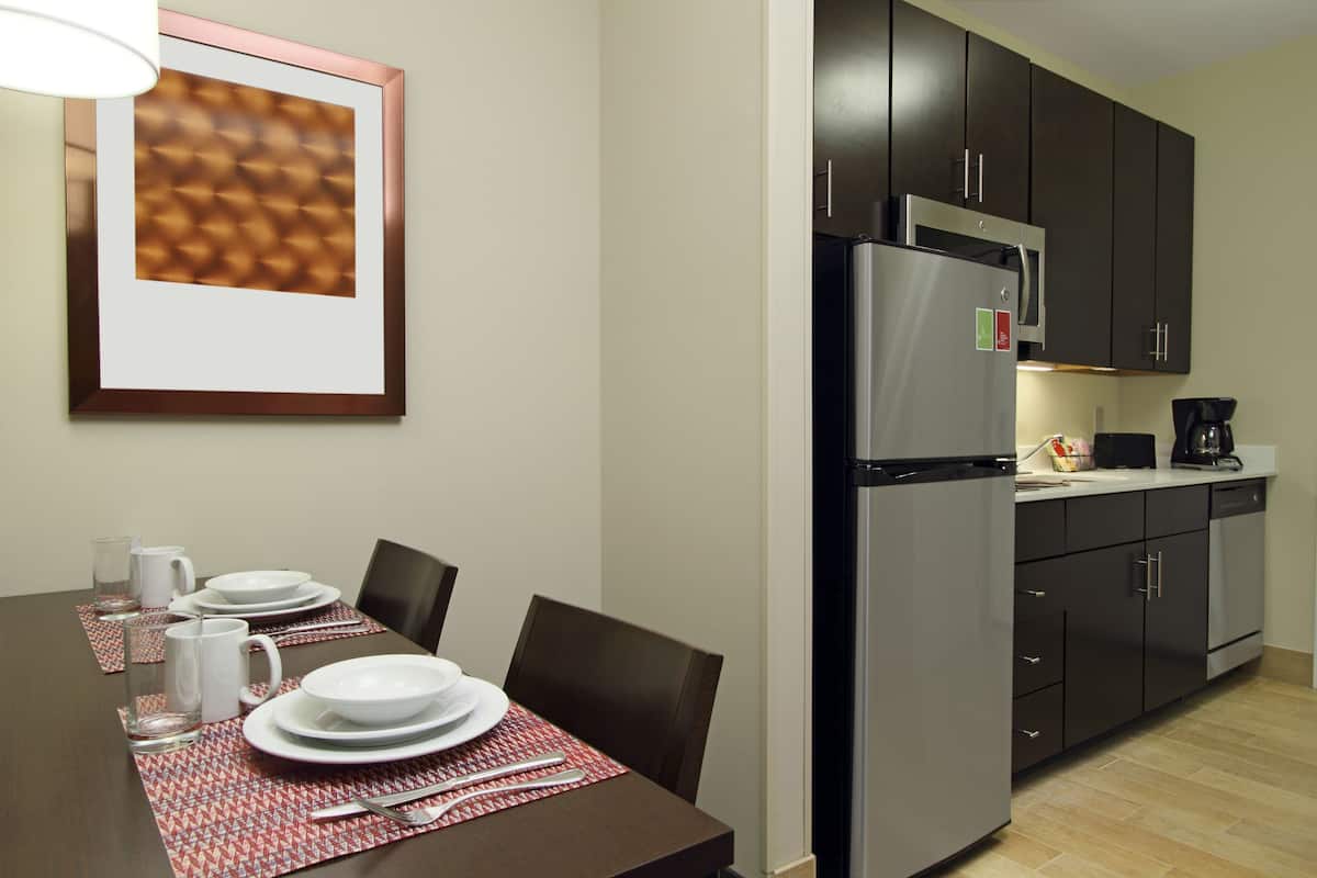 A dining area with a table set for four, a refrigerator, and dark cabinets.