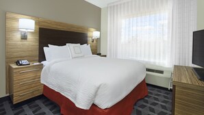 A hotel room with a large bed, two bedside tables with lamps, a television, and a window with curtains.