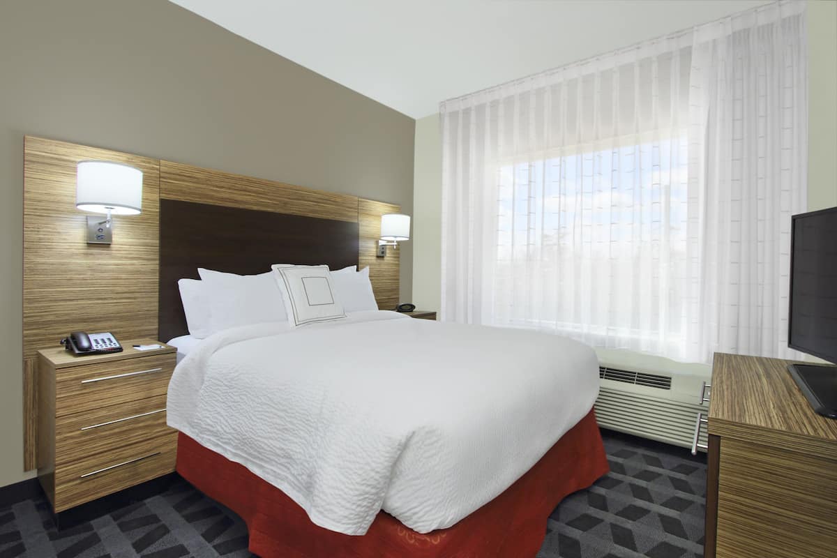 A hotel room with a large bed, two bedside tables with lamps, a television, and a window with curtains.