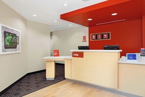 A reception area with a red accent wall, a 'Hello' sign, and a digital screen displaying information. - TownePlace Suites New Orleans Harvey/West Bank (Harvey)