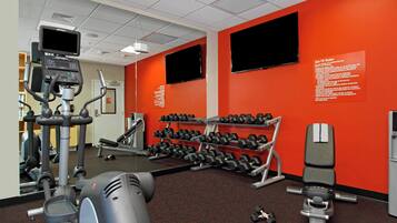 A gym with exercise equipment, dumbbells, and a red wall with a sign.