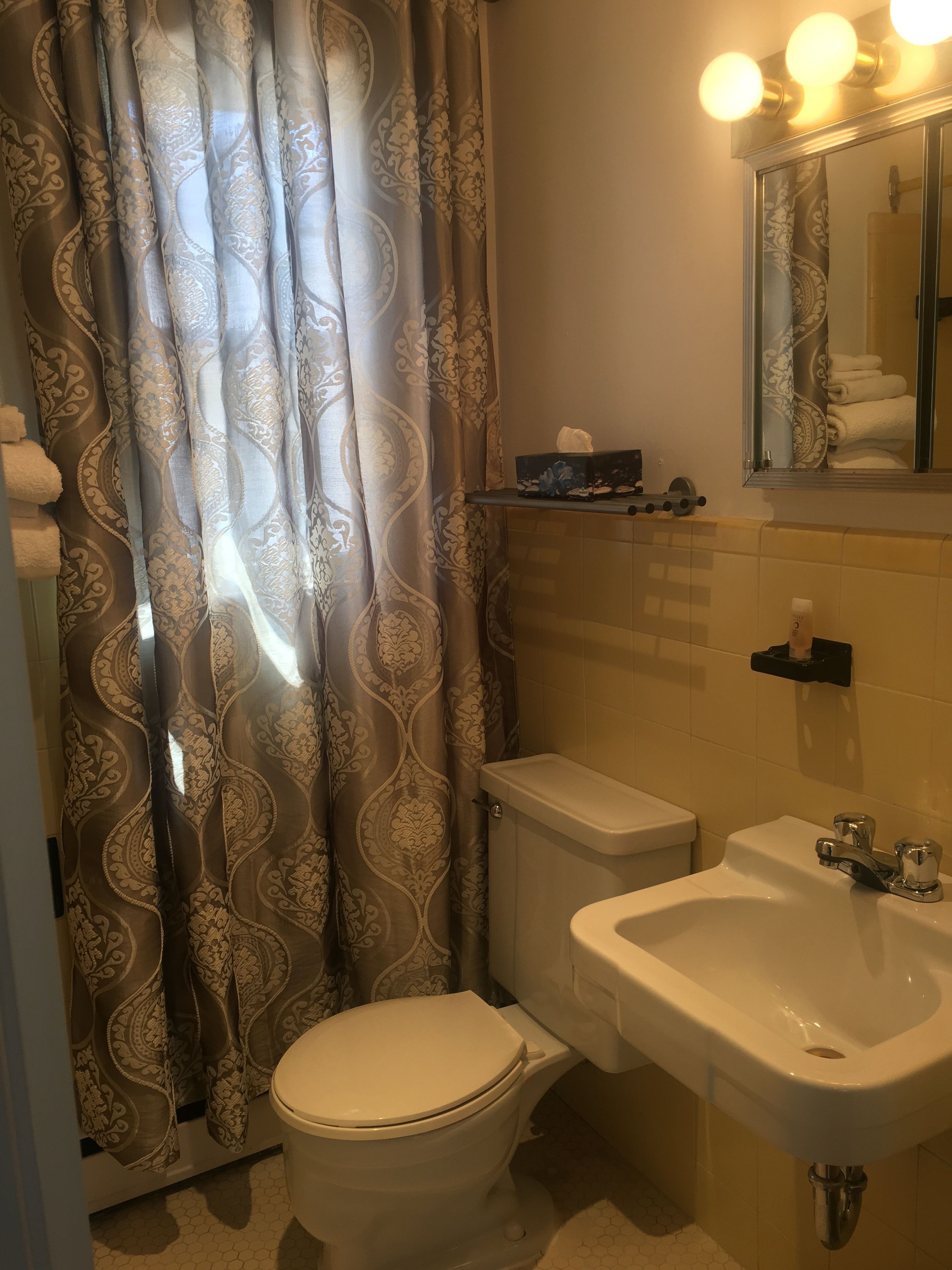 A bathroom with a toilet, sink, and a mirror with lights above.