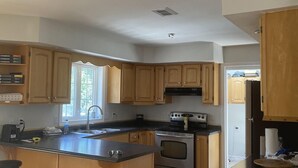 A kitchen with wooden cabinets, a central island with stools, a stove, and a refrigerator.