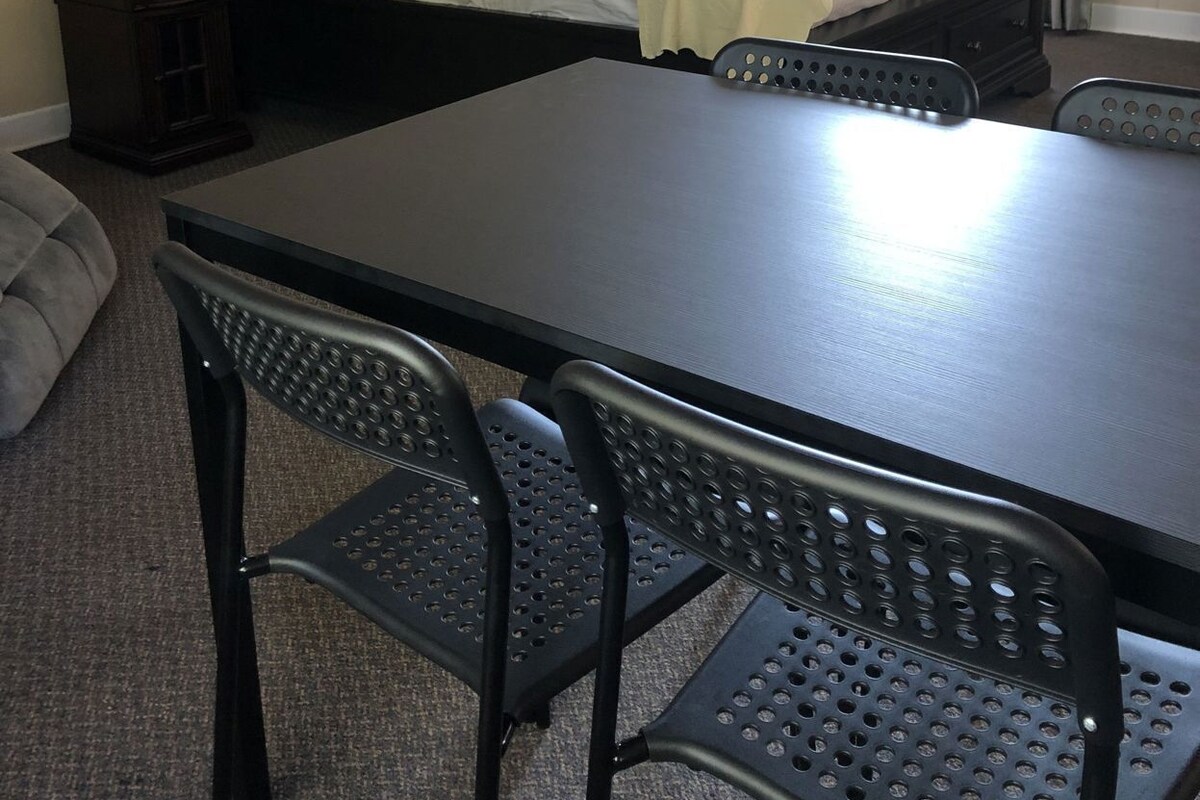 Una habitación de hotel con cama, mesitas de noche, un escritorio con sillas y una ventana con cortinas.