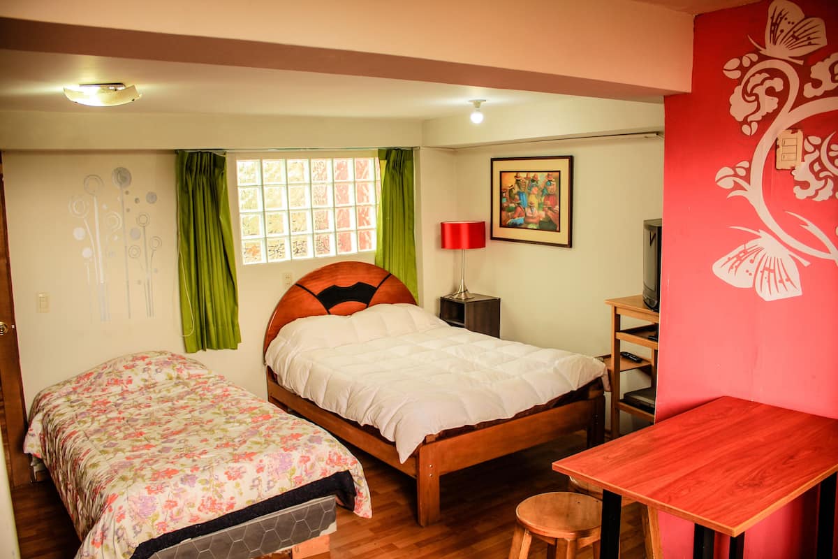 Une chambre avec deux lits, une table en bois, une chaise, un téléviseur et un élément de décoration rouge sur le mur.