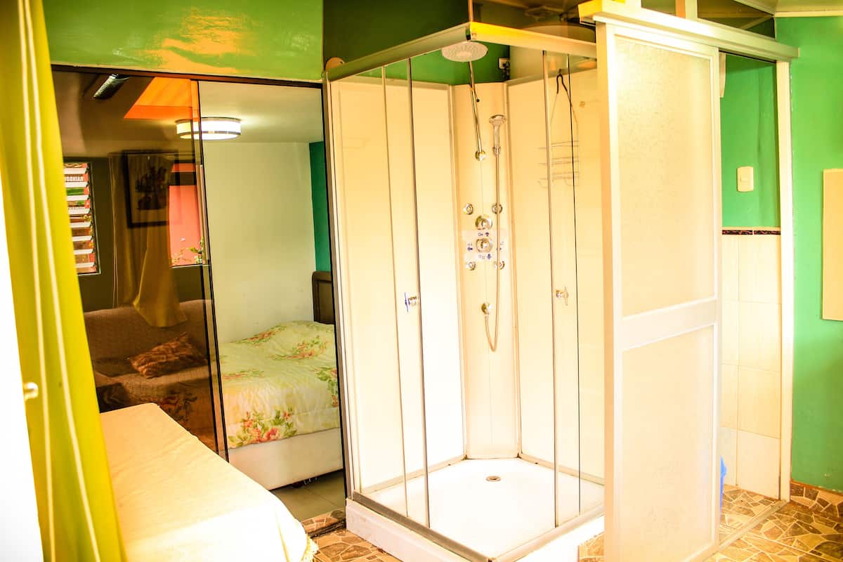 Une chambre dotée d’une douche en verre, d’un lit avec une literie à motifs floraux et d’un mur vert.