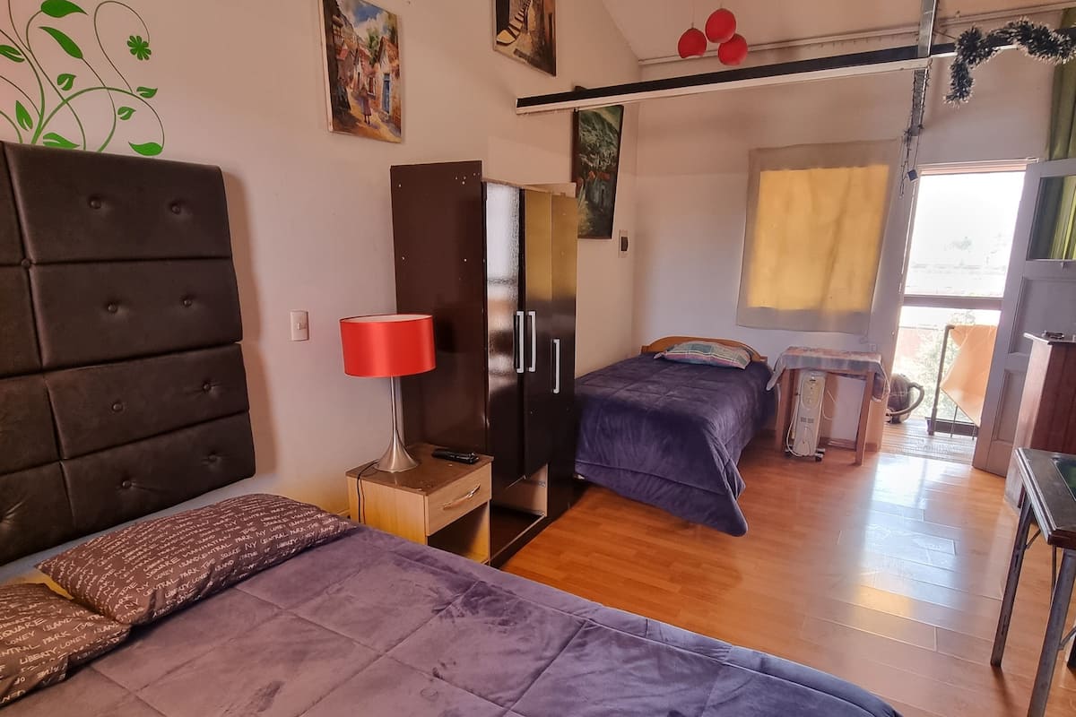 Une chambre avec deux lits, un bureau, une chaise, une lampe et une fenêtre.