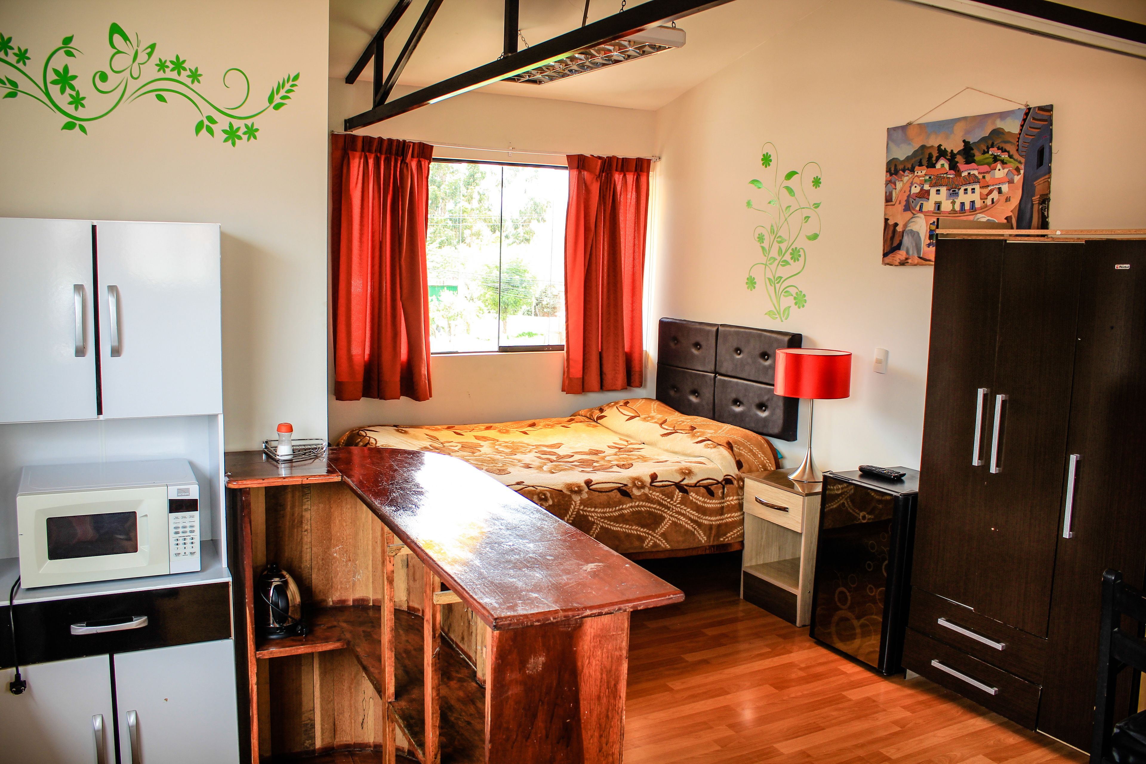 Habitación compacta con cama, escritorio de madera, armario, microondas y un cuadro en la pared.