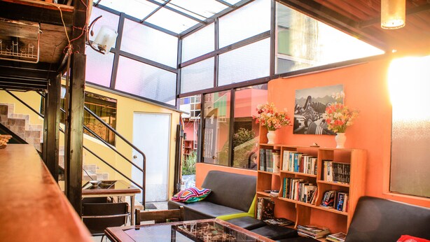 A cozy living area with a sofa, coffee table, and bookshelf, featuring a large window and a staircase. - Inkas Garden Apartment (Cusco)