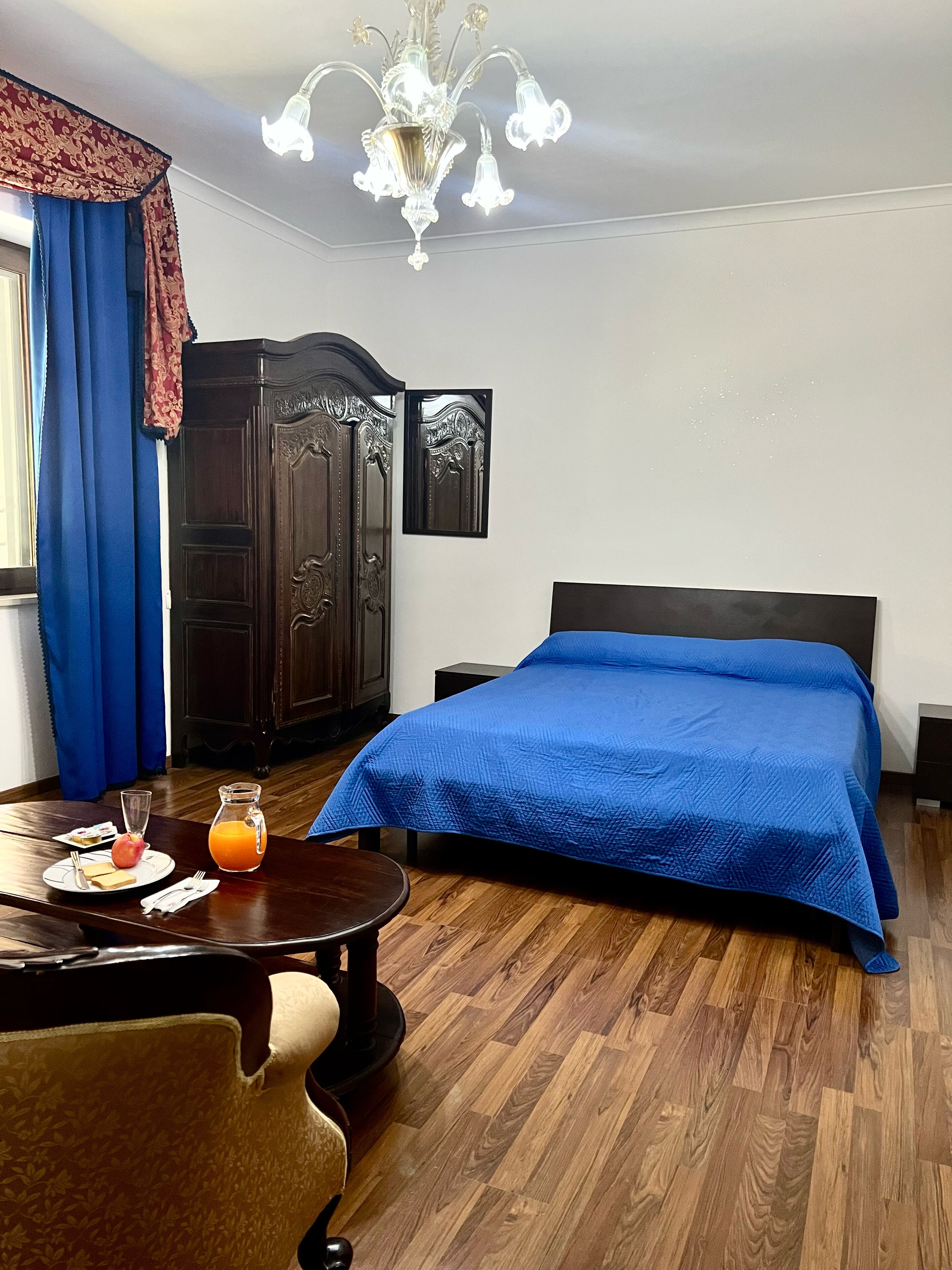 Habitación de hotel con cama, un armario de madera, una mesa de comedor con desayuno y una araña.