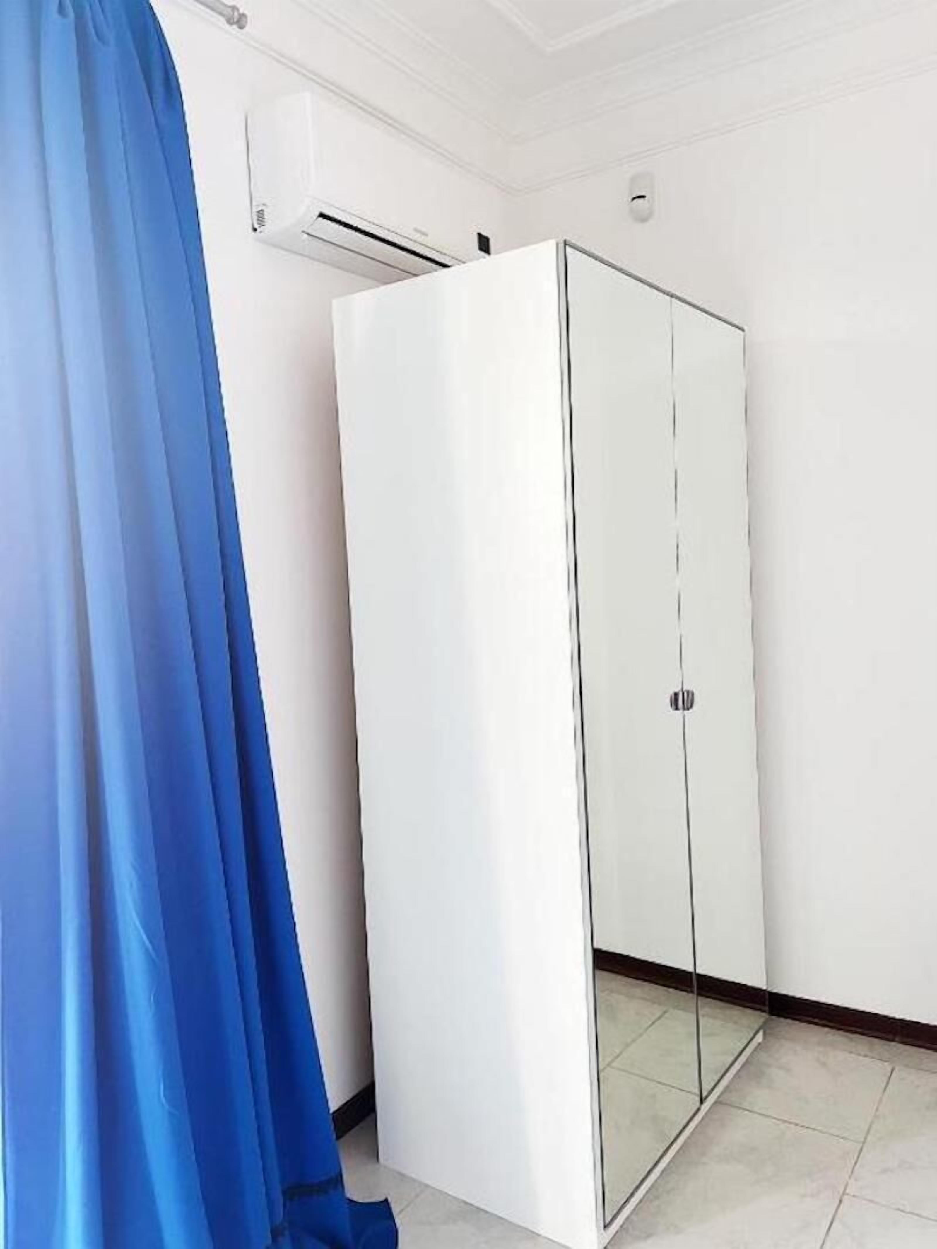 A room with a white wardrobe, a blue curtain, and an air conditioning unit on the wall.