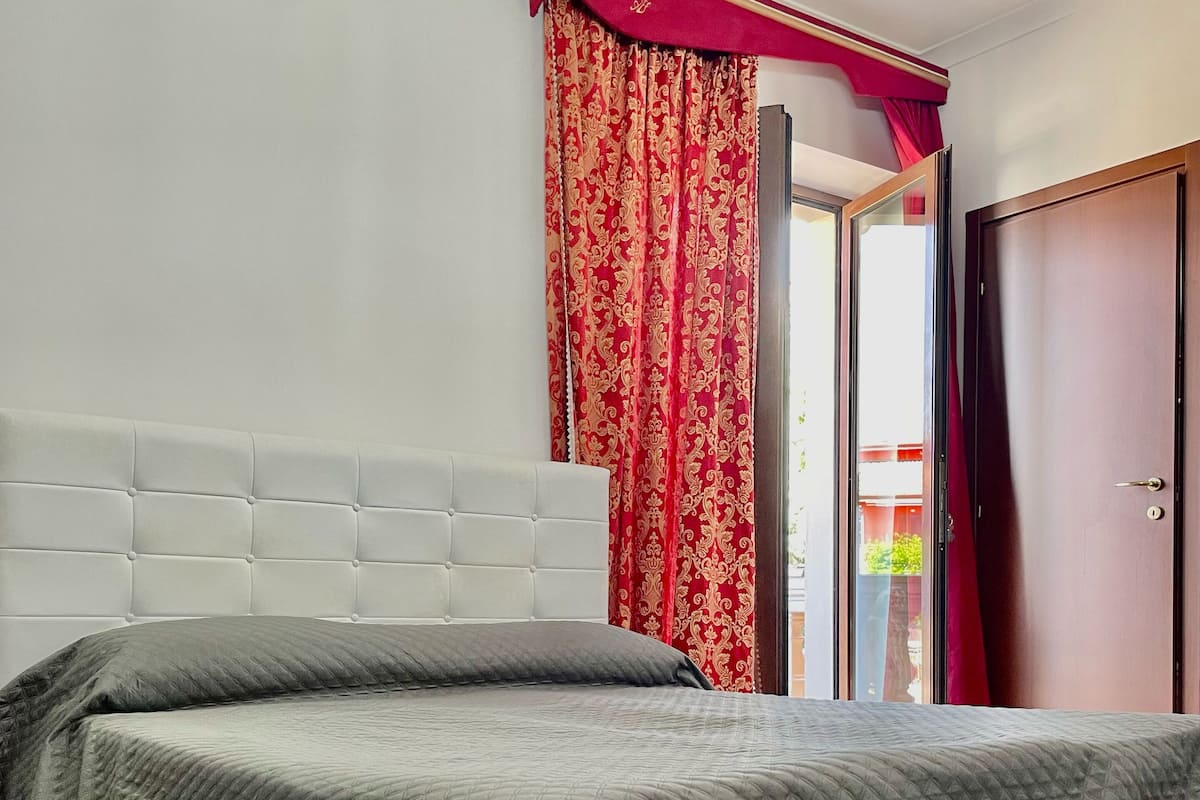 A bedroom with a white upholstered headboard, a grey quilted bedspread, and a wooden floor.