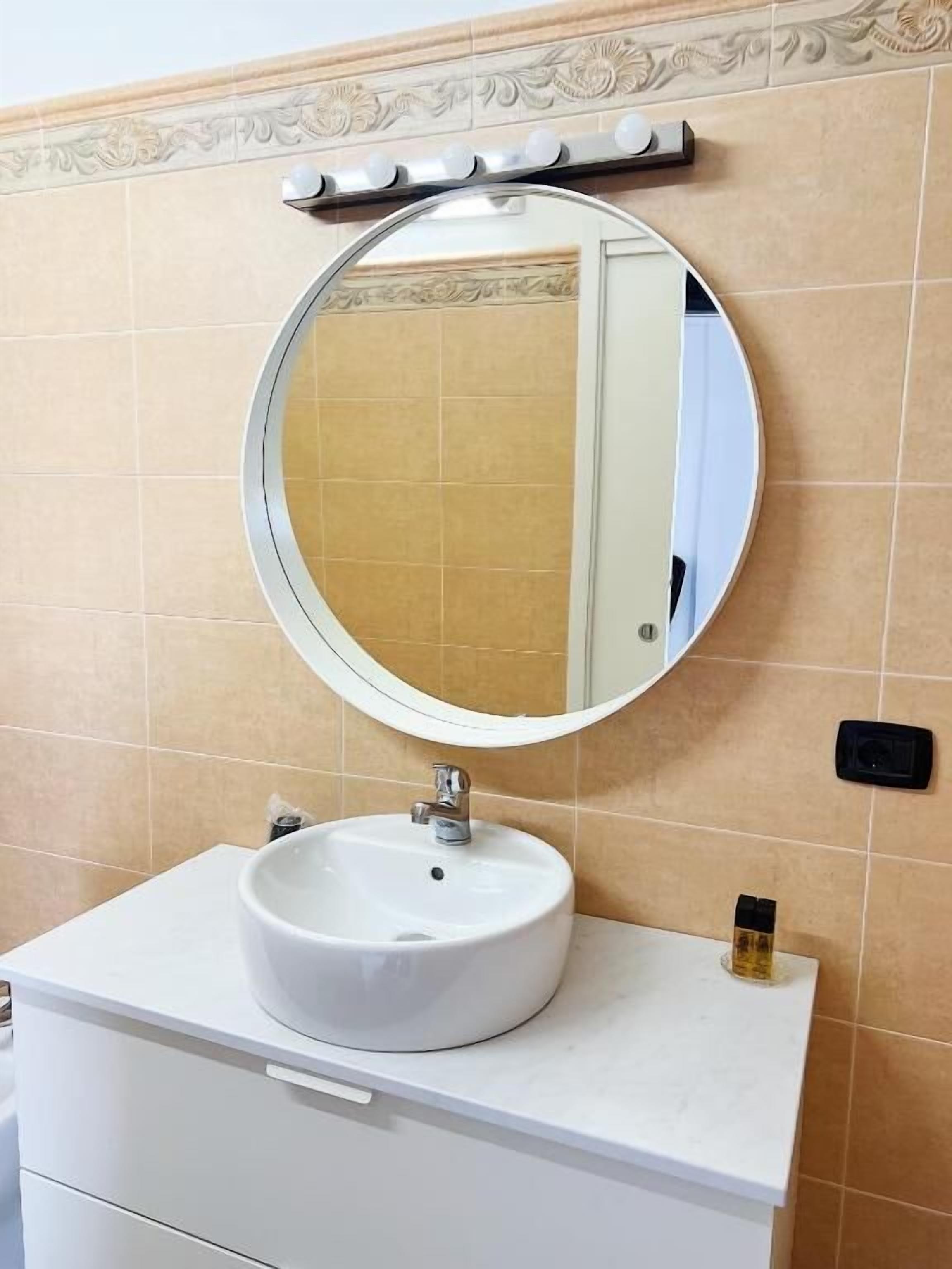 A bathroom with a round mirror, a white sink, and a vanity with a drawer.