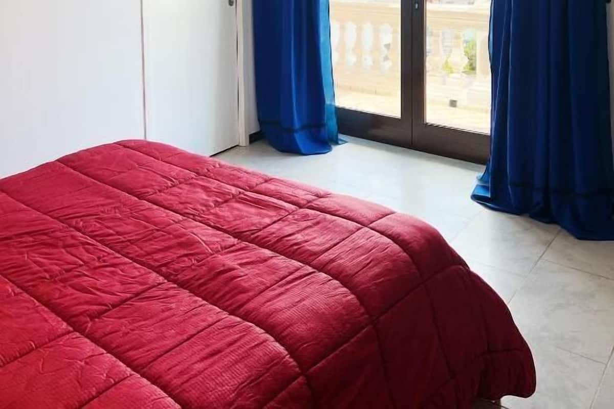A hotel room with a large bed, a flat-screen TV mounted on the wall, and a sliding glass door with blue curtains.