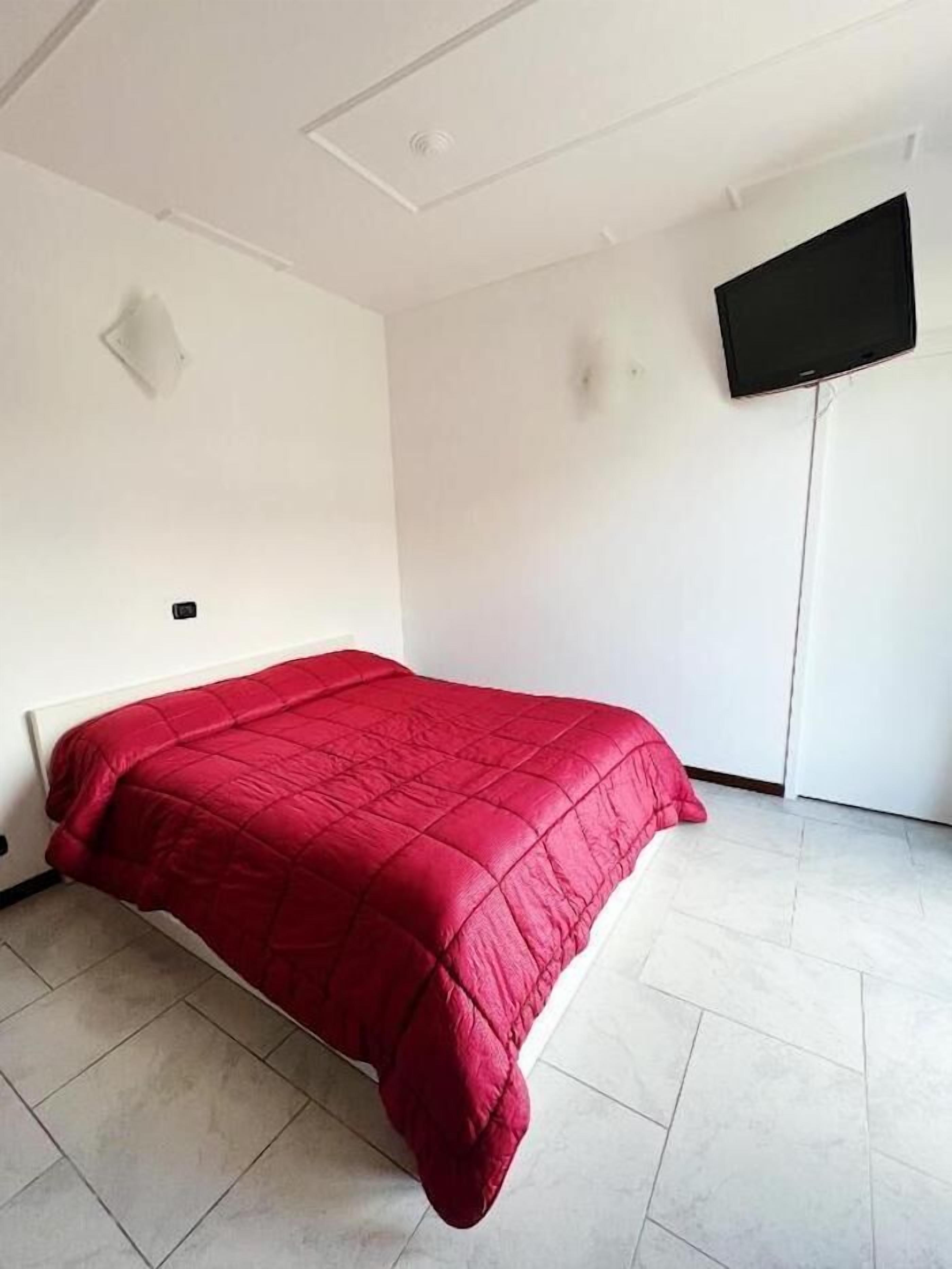 A room with a bed, white walls, a flat-screen TV mounted on the wall, and a tiled floor.
