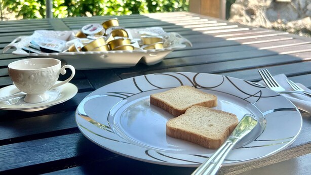 A table set with a plate of toast, a cup, and a tray of pastries, with a stone sculpture and greenery in the background. - Lo Scrigno B&B (Montemiletto)