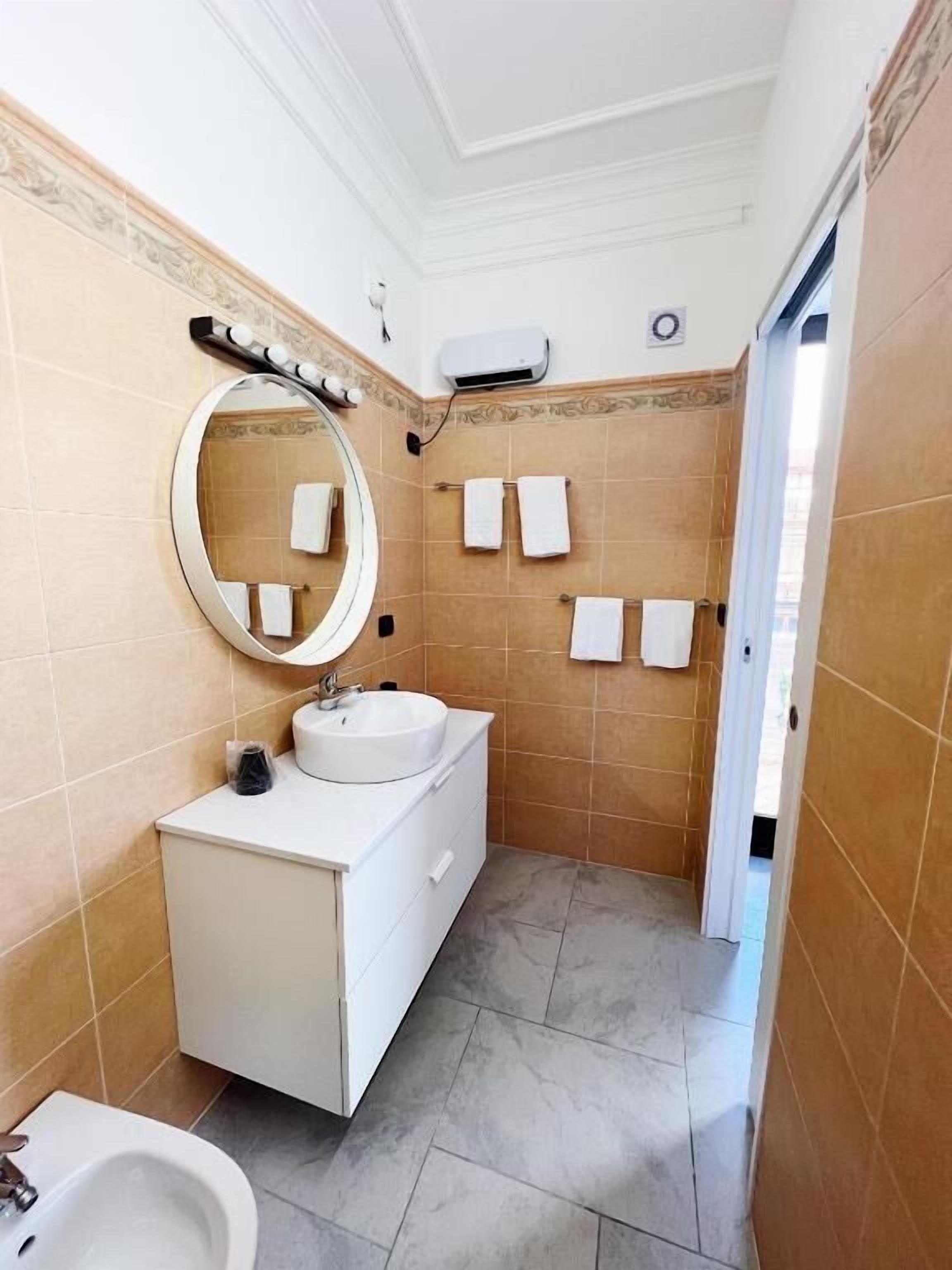 A bathroom with a white vanity, a round mirror, a sink, and a bidet.