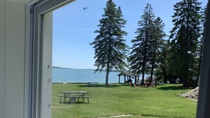 Une vue depuis une fenêtre donnant sur un espace verdoyant avec des tables de pique-nique et un kiosque, avec un lac et des arbres en arrière-plan.