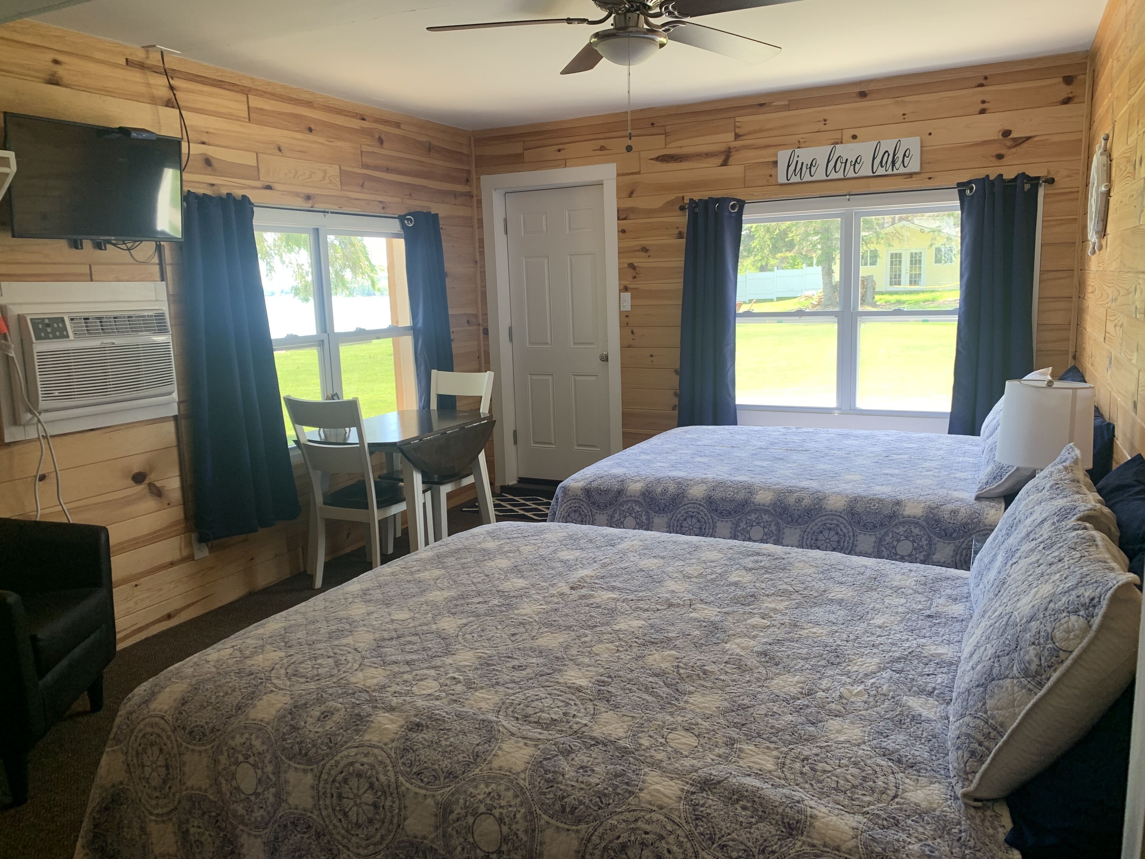 A cabin with two beds, a dining table, chairs, a TV, and a sign that reads "live love lake".