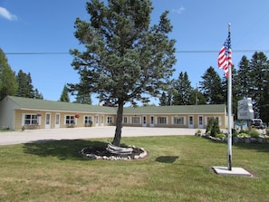 Ein Motel mit einer Reihe von Zimmern, einer Fahnenstange mit der amerikanischen Flagge und einem großen Baum im Vorgarten.