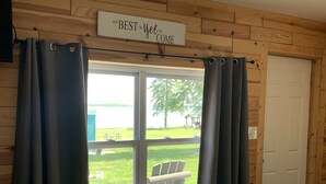 Une pièce de style cabane en bois, avec un lit, une fenêtre avec des rideaux et une pancarte au-dessus de la fenêtre sur laquelle on peut lire : « Le MEILLEUR est encore à venir ».