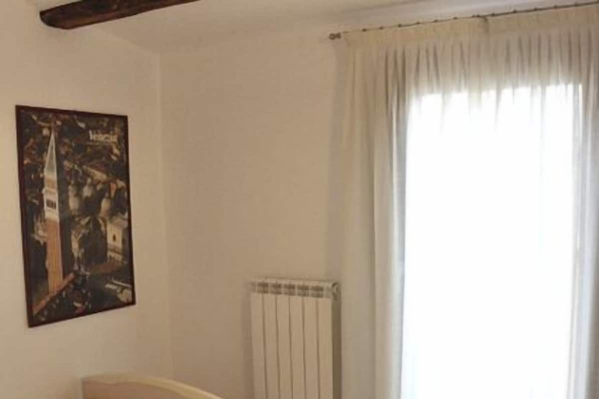 Een slaapkamer met een enkel bed, een radiator, een raam met gordijnen en een poster aan de muur.