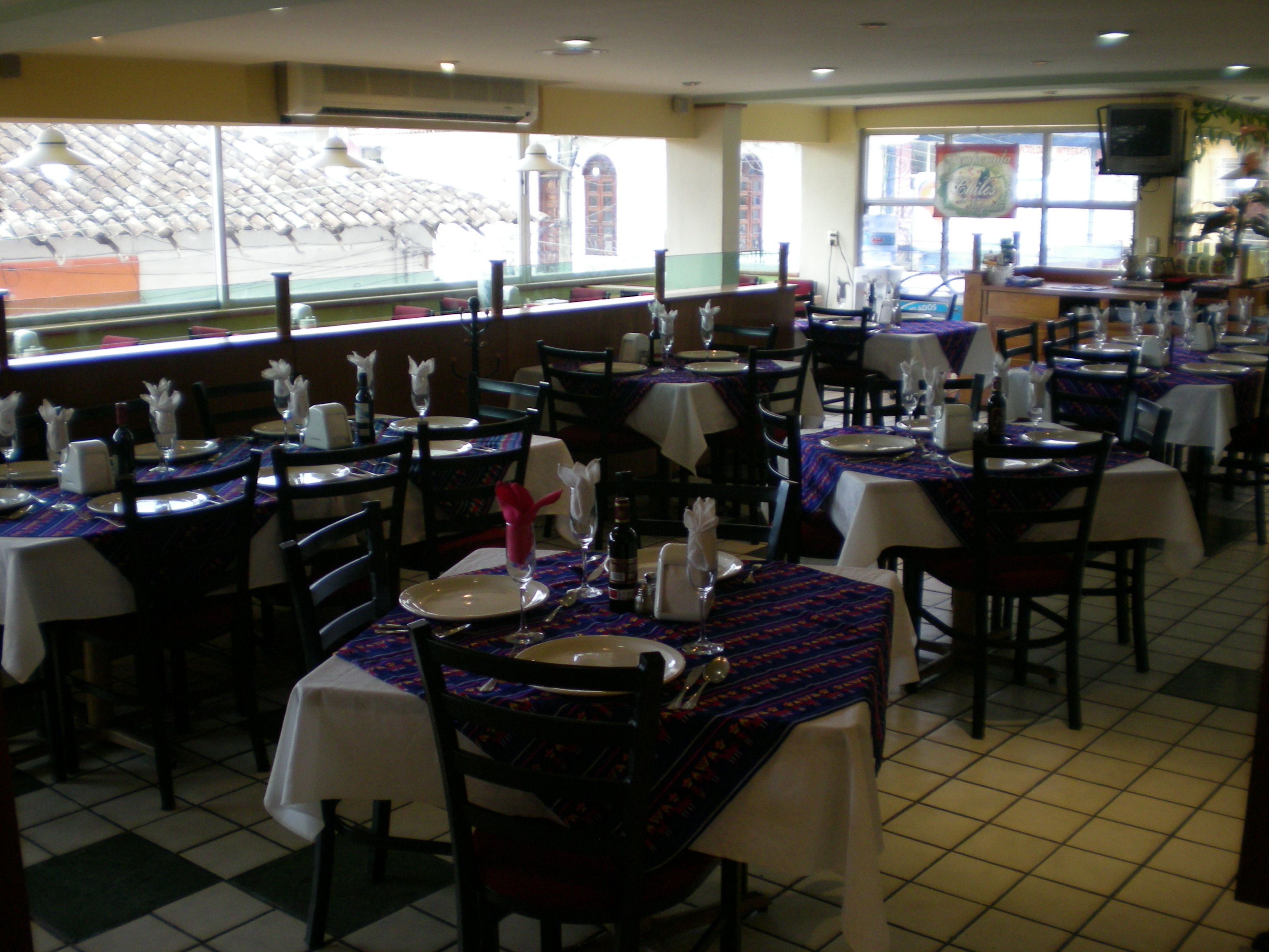 A restaurant with multiple tables set for dining, featuring patterned tablecloths and chairs.