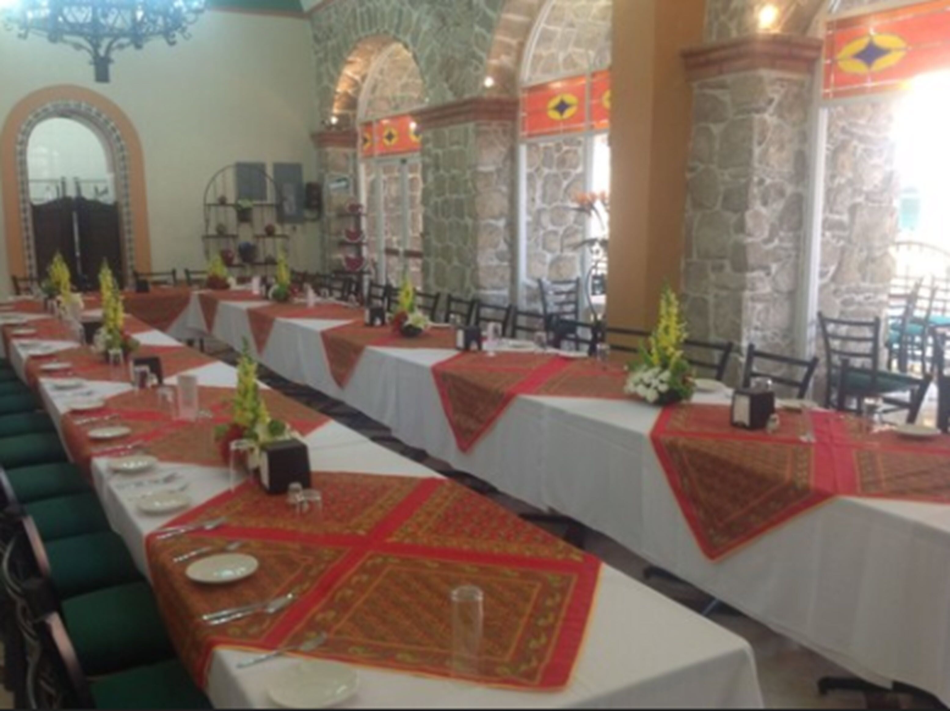 Una larga mesa de comedor con manteles blancos y caminos de mesa rojos, dispuesta con platos, cubiertos y pequeñas macetas.