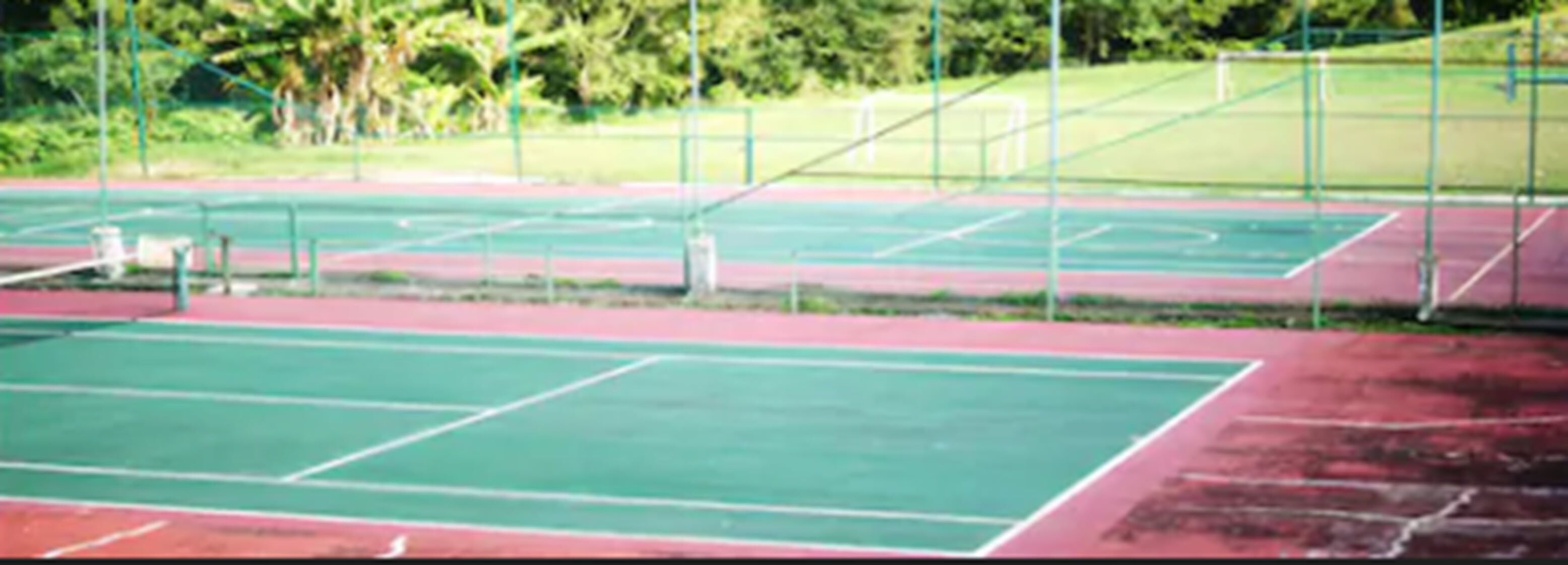 A tennis court with multiple green courts and a red track.