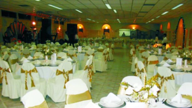 A banquet hall with round tables set for a formal event, featuring white tablecloths and gold sashes on chairs. - Hotel Tajín (Papantla de Olarte)