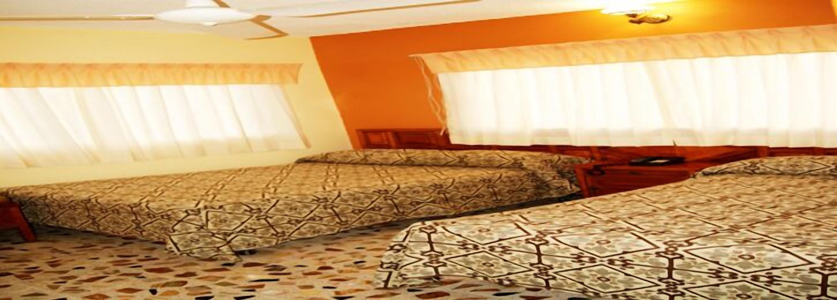 Habitación con dos camas, cada una con ropa de cama estampada, un ventilador de techo y una ventana con cortinas.