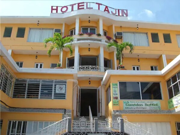 A hotel with a yellow facade, balconies with railings, and a sign for 'Comidas Buffet'.