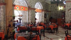 Un restaurante con paredes de piedra, ventanas arqueadas y mesas cubiertas con manteles anaranjados.