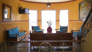 Un vestíbulo con un banco de madera, dos sillones azules, un jarrón rojo con flores y un cuadro en la pared.
