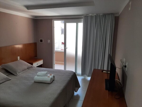 Habitación de hotel con cama, escritorio, televisor y puerta corrediza a un balcón.