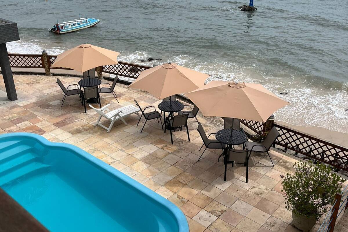 Uma área à beira da piscina com mobiliário externo e vista para o mar.