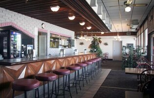 Zona de bar con mostrador, varios taburetes y una cocina al fondo.