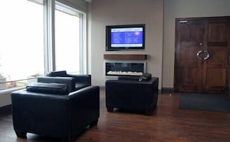 Ein modernes Wohnzimmer mit großem Fenster, einem wandmontierten Flachbildfernseher und einer Holztür.
