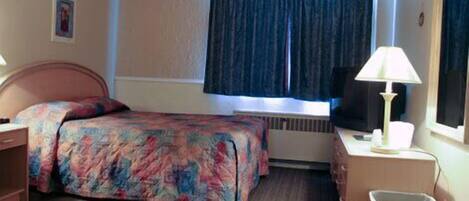 A hotel room with a bed, a desk with a lamp, a chair, and a window with curtains.