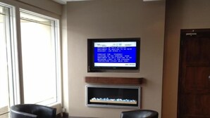 Un vestíbulo moderno con un televisor de pantalla plana montado en la pared, dos sillones de cuero, una chimenea y un piso de madera.
