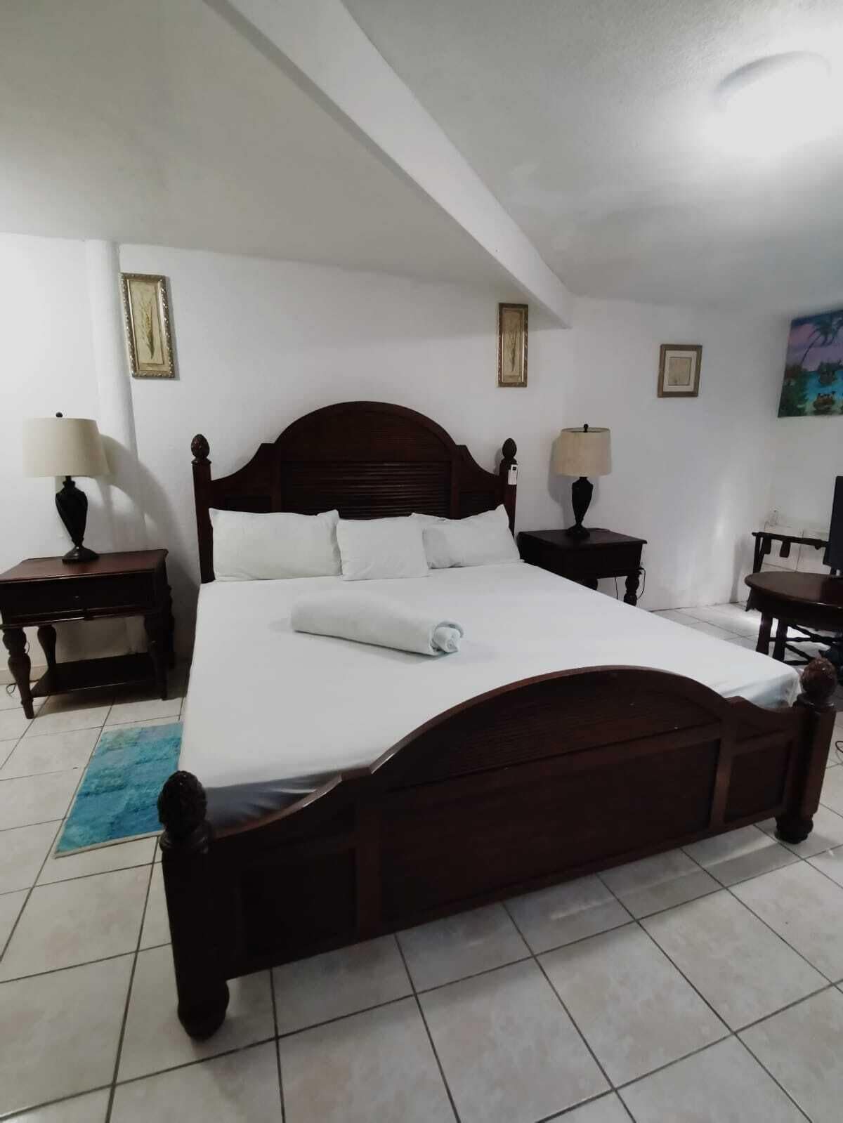 A neatly made bed in a room with white walls, a wooden headboard, and two bedside tables with lamps.